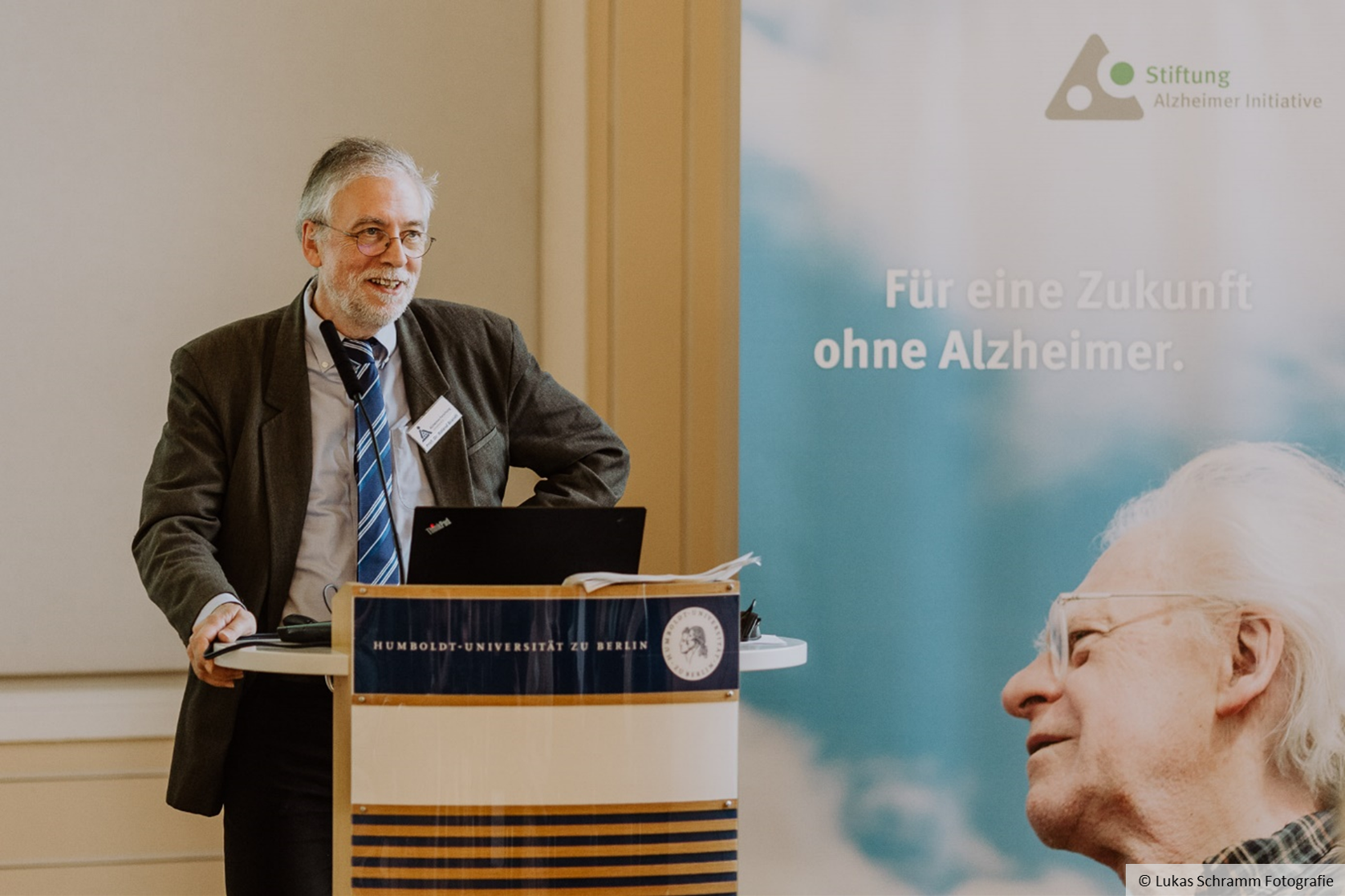 Roland Brandt steht an einem Redepult, neben ihm ist ein Plakat mit dem Schriftzug "Für eine Zukunft ohne Alzheimer" zu sehen.