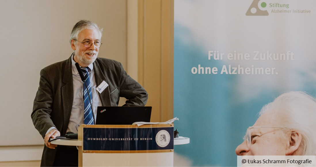 Roland Brandt steht an einem Redepult, neben ihm ist ein Plakat mit dem Schriftzug "Für eine Zukunft ohne Alzheimer" zu sehen.