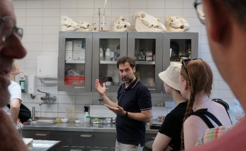 Chadi Touma steht vor Studierenden in einem Labor und scheint etwas zu erklären. Im Hintergrund sind Tierschädel zu erkennen.