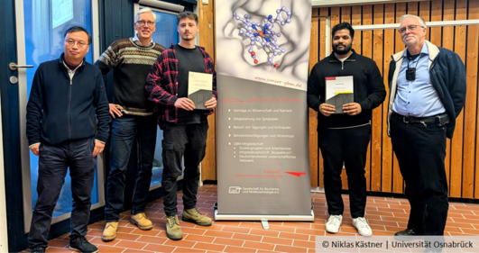 Five people smile into the camera. The two in the centre hold certificates in their hands.